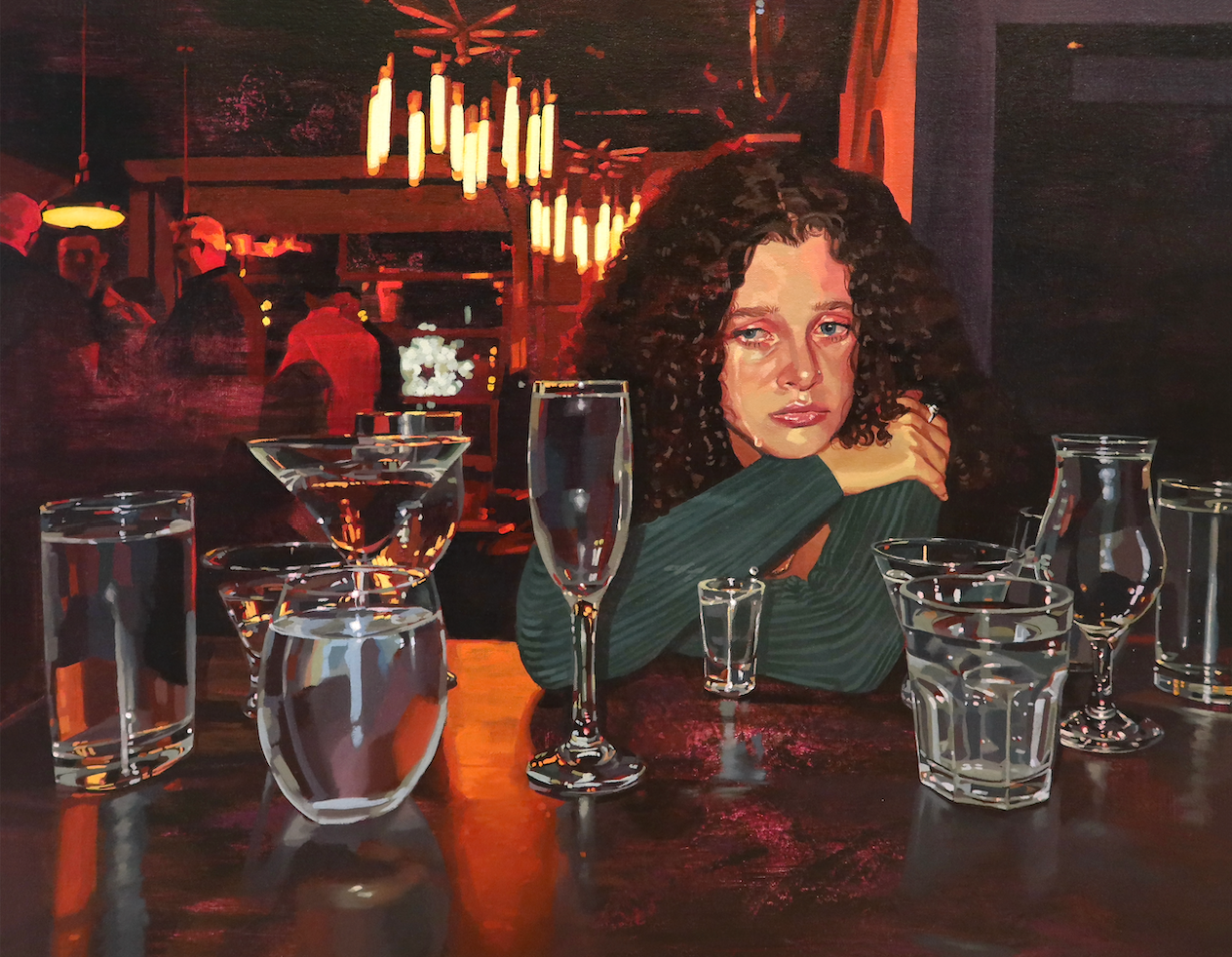 Painting of a white girl with thick brown curly hair wearing a deep green sweater crying at the bar surrounded by glasses of varying size and shape. One tear is seen falling into the shot glass in front of her. The lighting in this piece leaves the majority of the painting a red-tone.