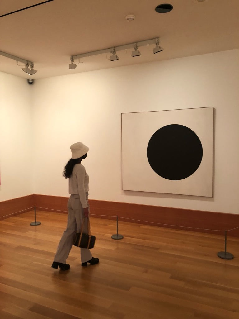 Women in a gallery looking at a minimalistic black circle painting.